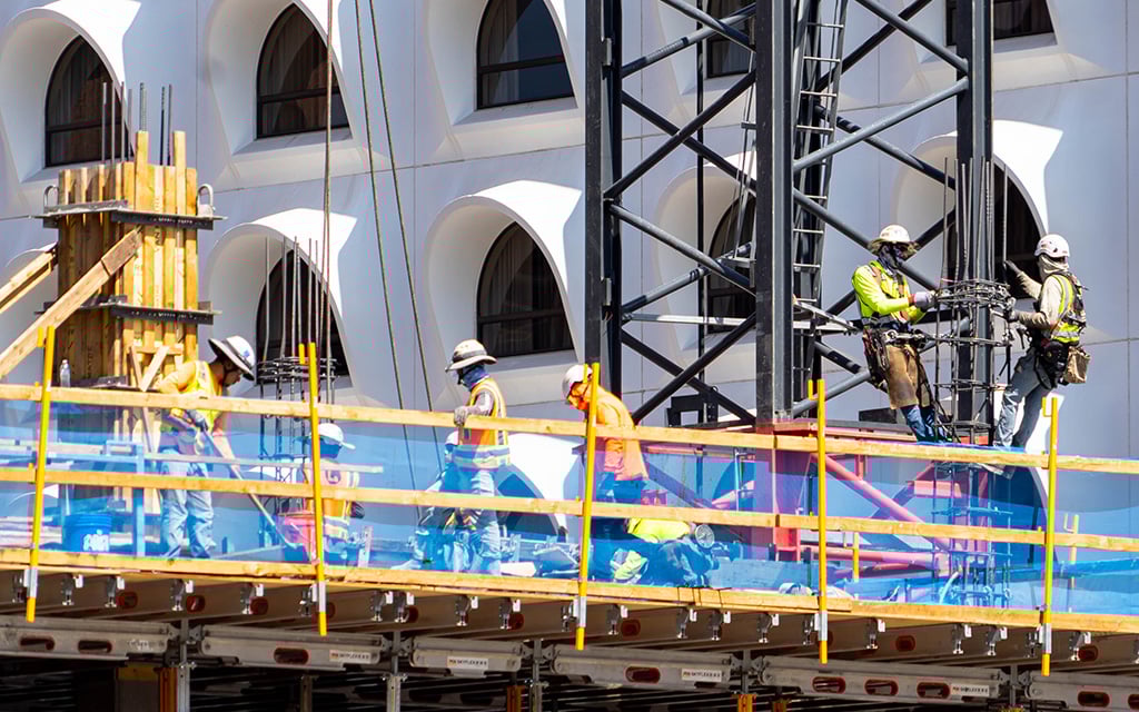 Construction workers on scaffolding in front of a vaulted building.