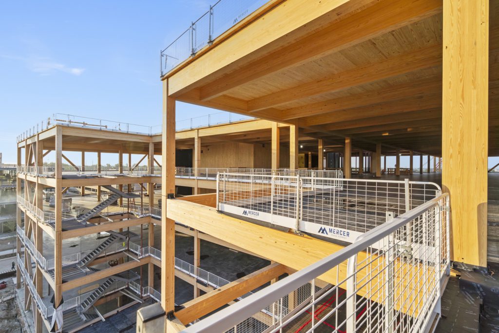 A partially built building that shows wooden beams, spacious open levels and safety railings against a clear blue sky.