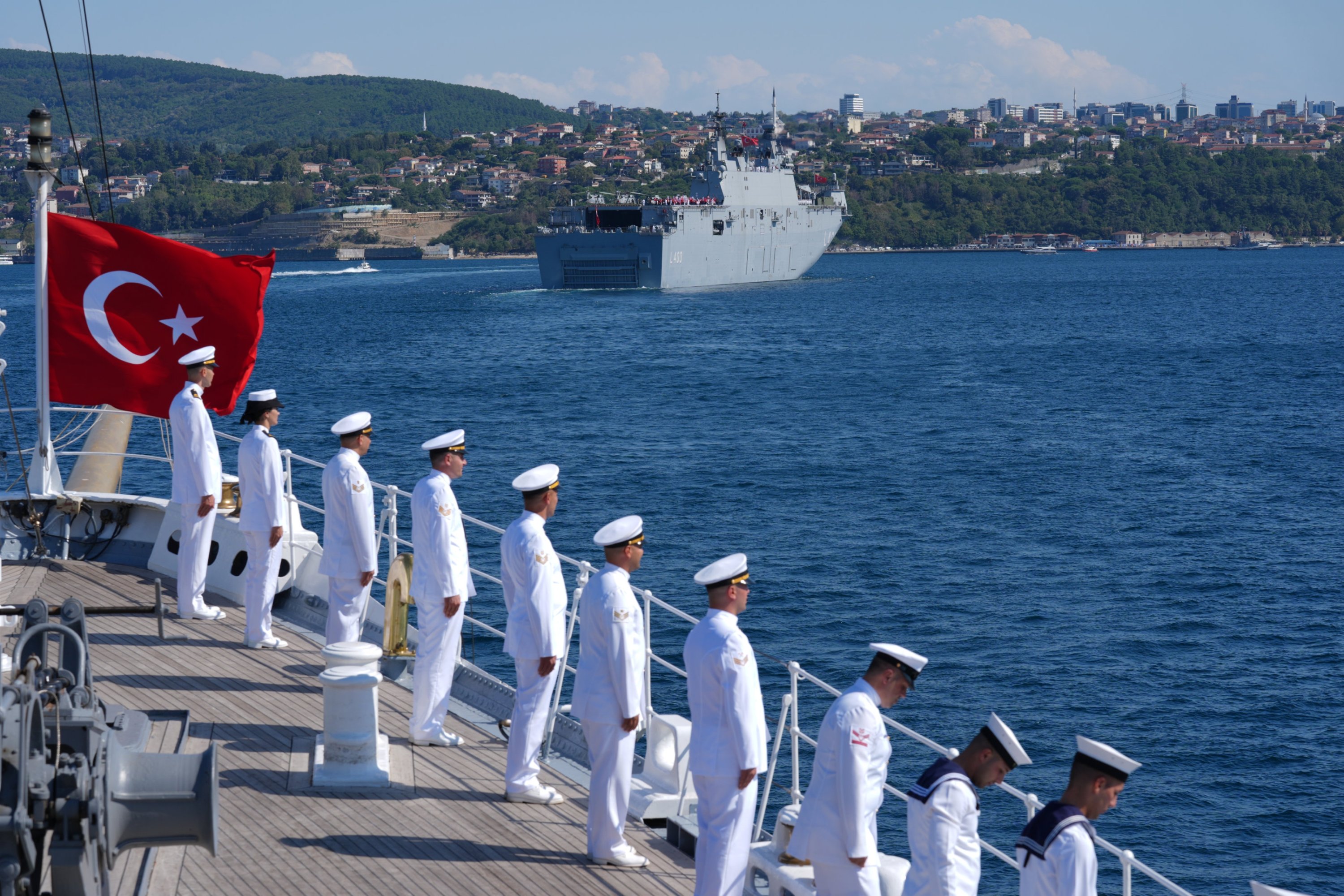 A Turkish flag and officers are seen on board a ship with a backdrop of a bridge during the Teknofest Blue Homeland Parade, Istanbul, Türkiye, August 24, 2025, (AA photo). (AA photo)